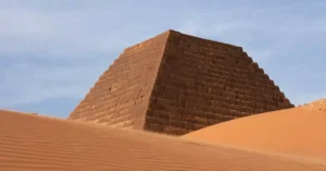 A striking image of an ancient pyramid amidst desert dunes under clear blue skies.