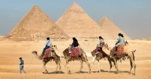 Tourists riding camels near the Great Pyramids of Giza, Egypt under clear skies.