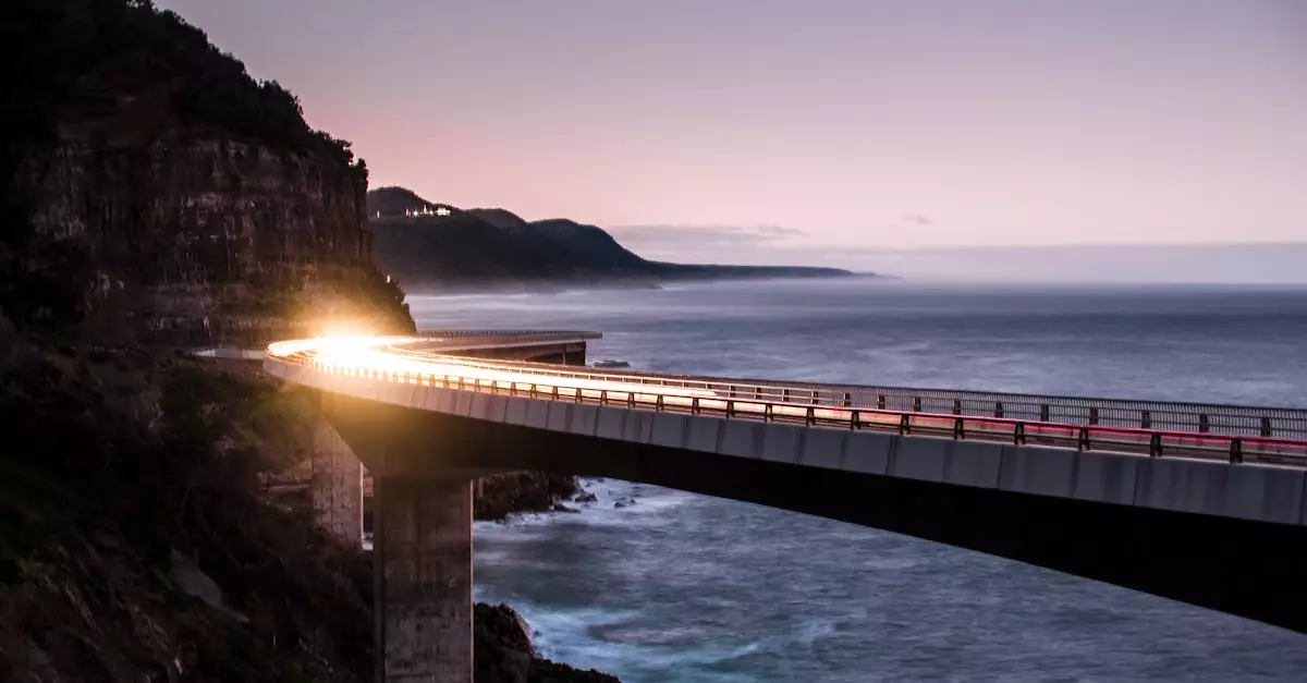 A stunning shot of the Sea Cliff Bridge near Wollongong, NSW at sunset, showcasing car light trails and scenic ocean views.