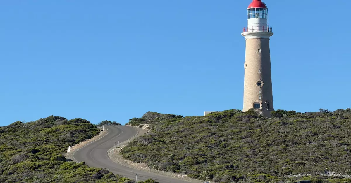 A towering lighthouse on Cape du Couedic stands against a clear blue sky, with lush greenery surrounding it.