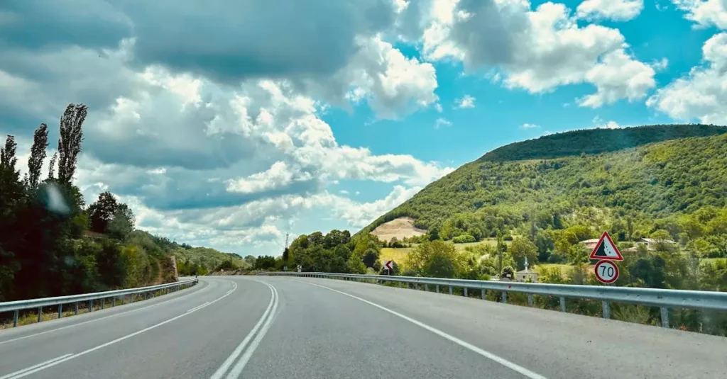 A picturesque highway winding through green hills under a bright blue sky with clouds.