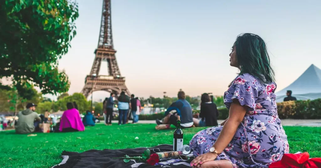 A woman enjoys a leisure picnic with wine in front of the Eiffel Tower on a sunny day in Paris.