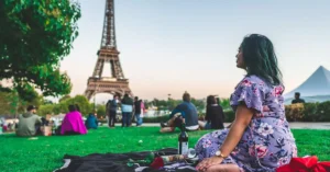 A woman enjoys a leisure picnic with wine in front of the Eiffel Tower on a sunny day in Paris.