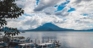 Boats docked with a stunning view of Lake Atitlan and its volcano under a cloudy sky.