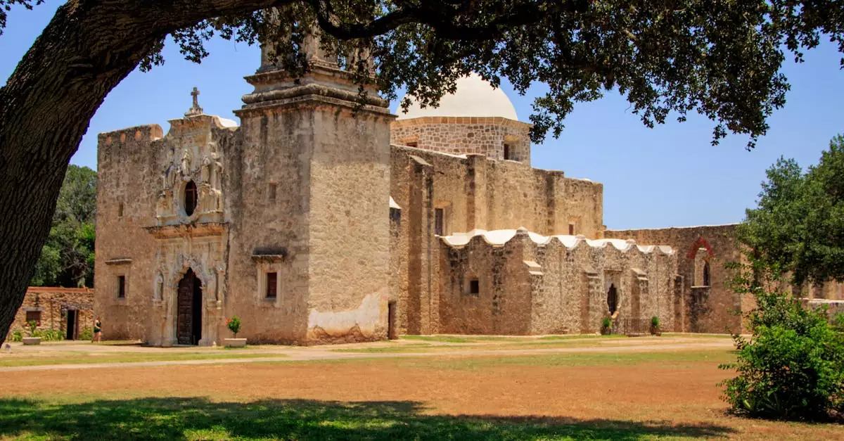 Statue of an old mission with lush trees in San Antonio, capturing historical architecture.