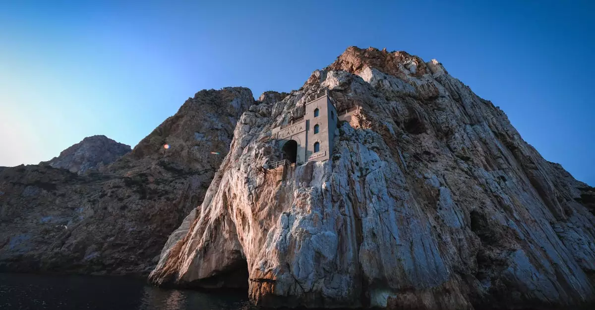 A historic structure built into a rocky cliff with a clear blue sky, near the sea.