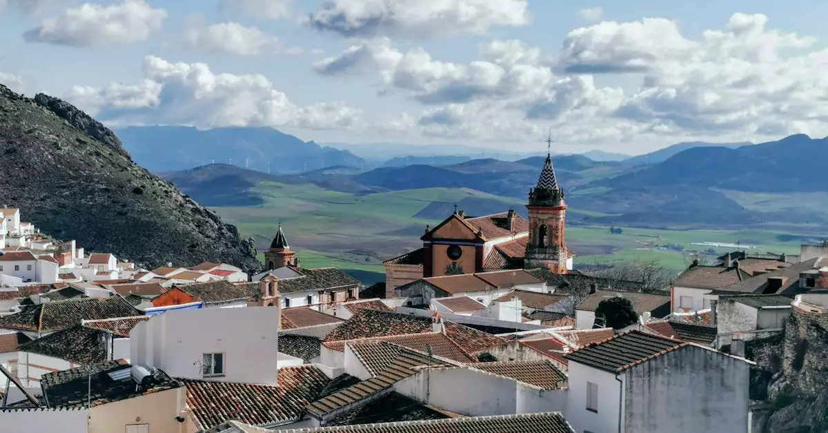 Discover the charming rooftops and majestic church in Ca&ntilde;ete la Real, Spain, against a mountainous backdrop.