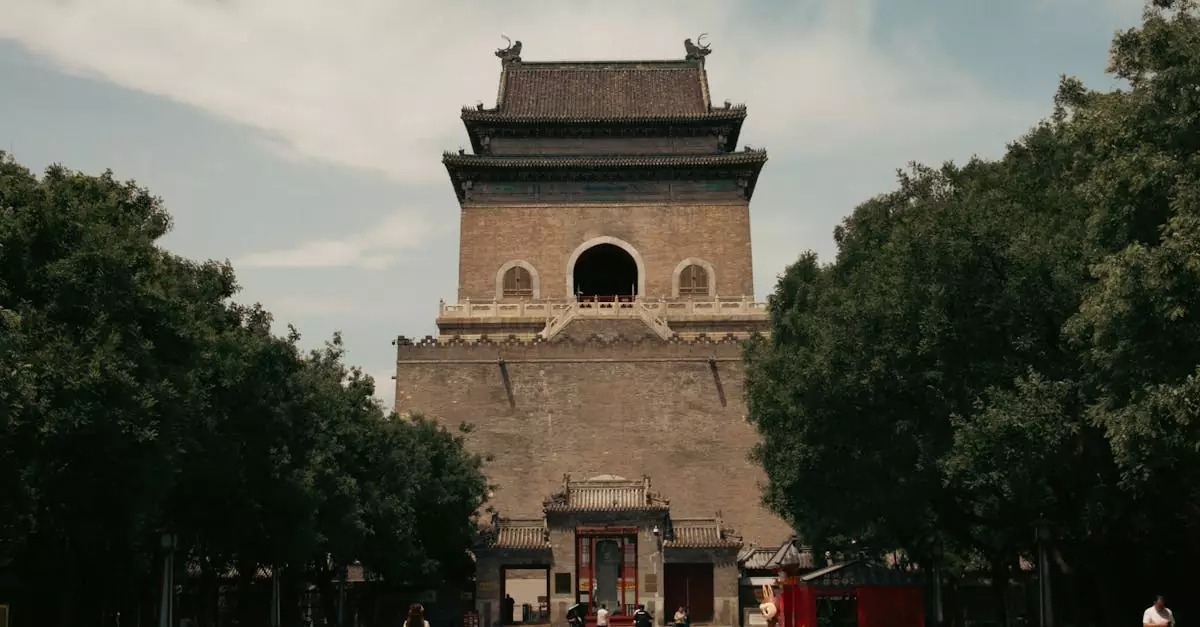A scenic view of the historic Bell Tower in Beijing, surrounded by trees and urban life.
