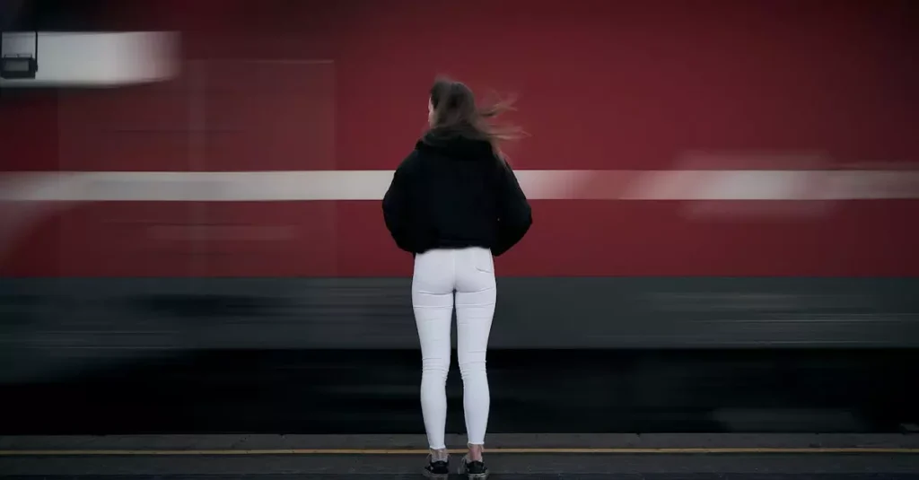 A woman standing at a train station in Leibnitz, Austria, as a red train passes by swiftly.