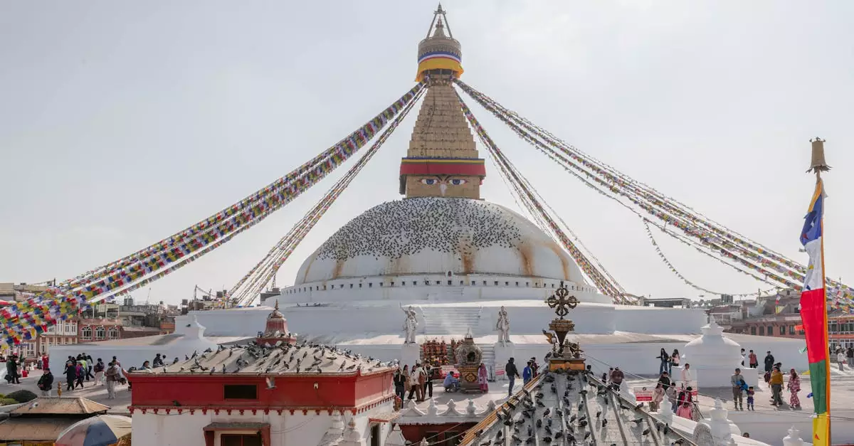 Boudhanath Stupa in Kathmandu with vibrant prayer flags and visitors on a sunny day, showcasing Nepalese culture.