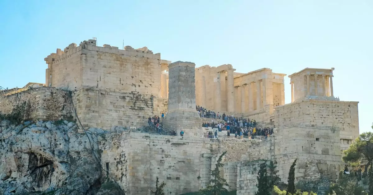 The ancient Acropolis of Athens with tourists on a sunny day, showcasing the Parthenon's grandeur.