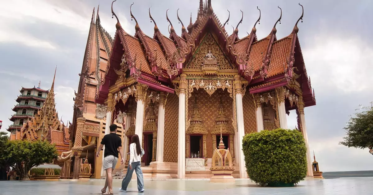 Couple walking by a traditional Thai temple with ornate architecture under a cloudy sky.