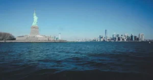 Picturesque cityscape with famous Statue of Liberty and modern skyscrapers of Manhattan located on river bank against cloudless blue sky in New York