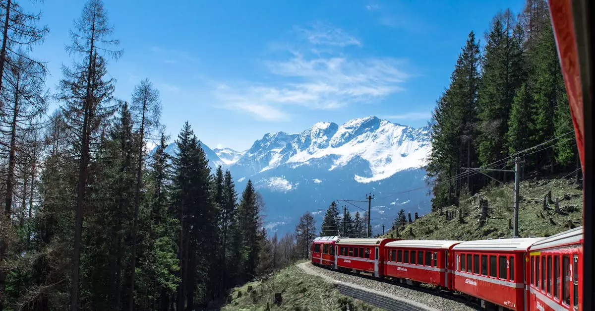 A red train travels through lush forests and snowy mountains under a clear blue sky in Switzerland.