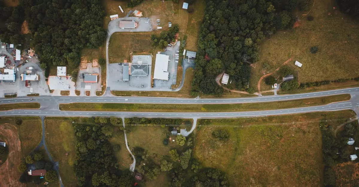 Overhead view of wavy roadways between green meadows with building roofs and trees in suburb