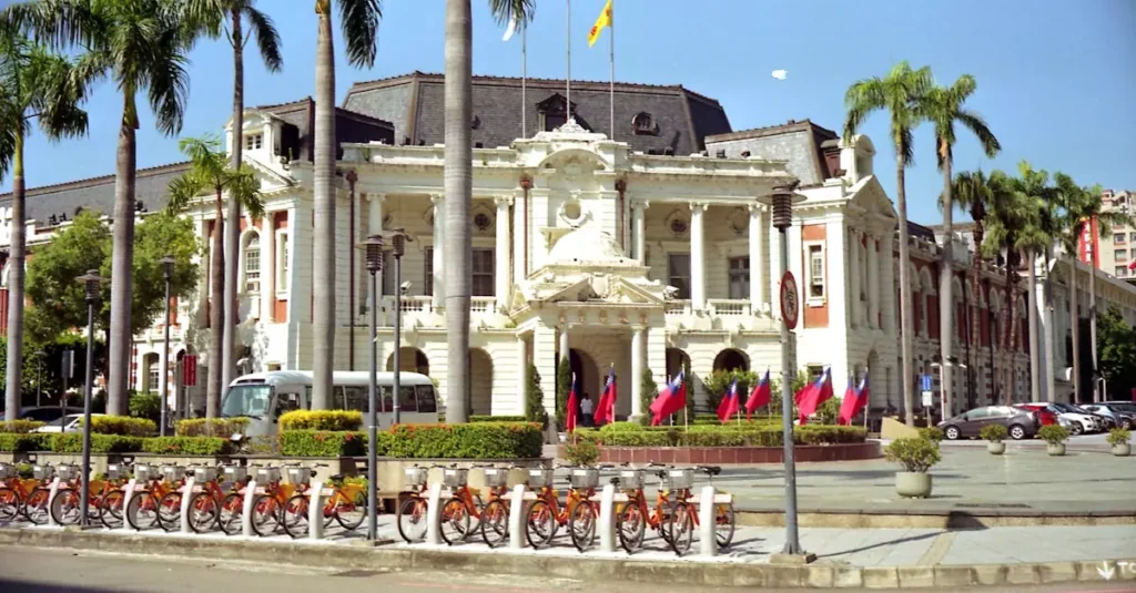 View of Taichung City Hall surrounded by palm trees and bicycles, under a clear blue sky.