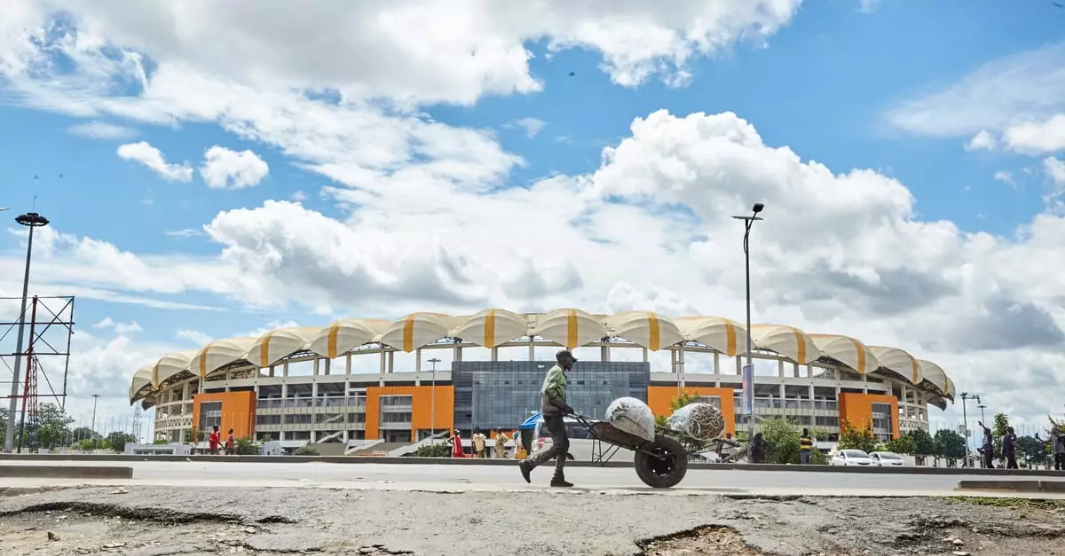 A person with a wheelbarrow in front of Lusaka Stadium under a blue sky with clouds.