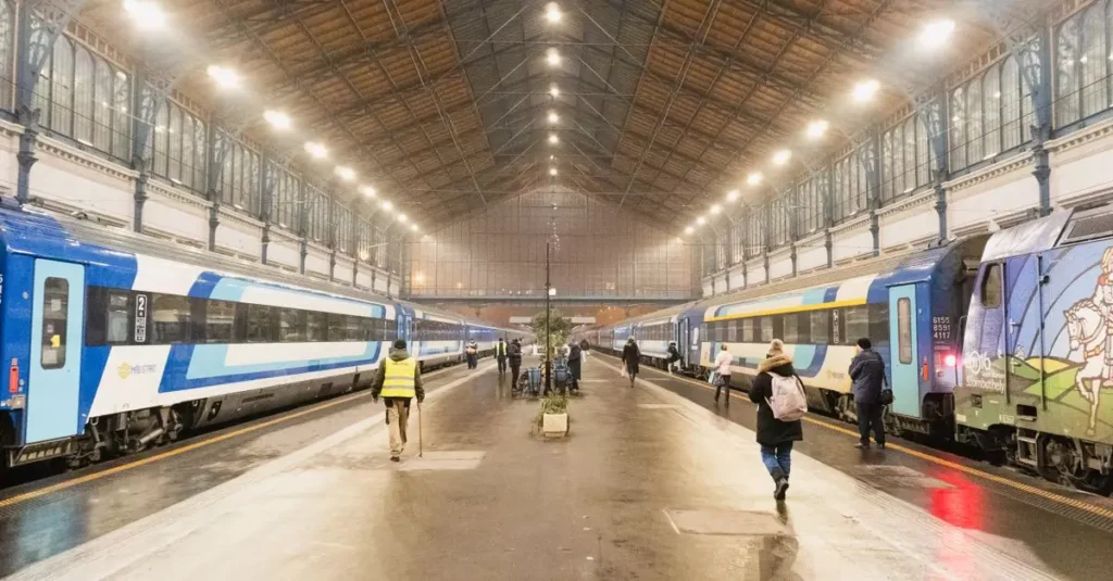 Busy scene at Nyugati Railway Station, Budapest with trains and commuters under iconic architecture.