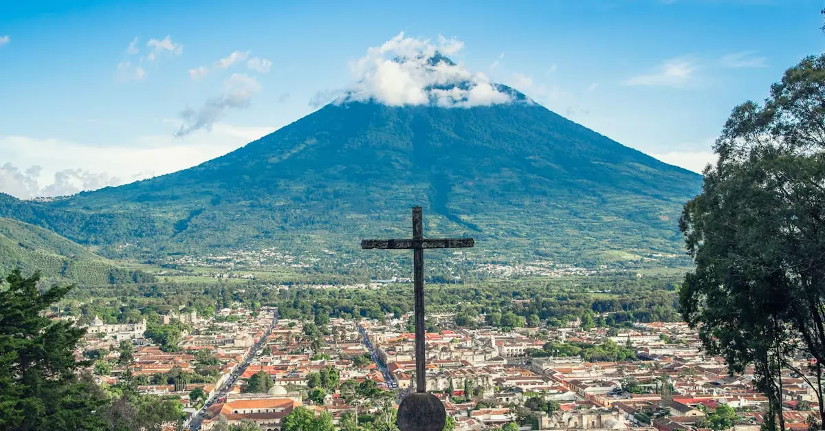 Scenic view of Antigua Guatemala with Volcán de Agua, featuring a prominent cross in the foreground.