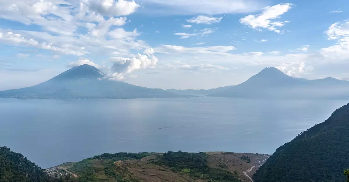 A stunning landscape of Lake Atitlán with surrounding volcanoes under a cloudy sky.