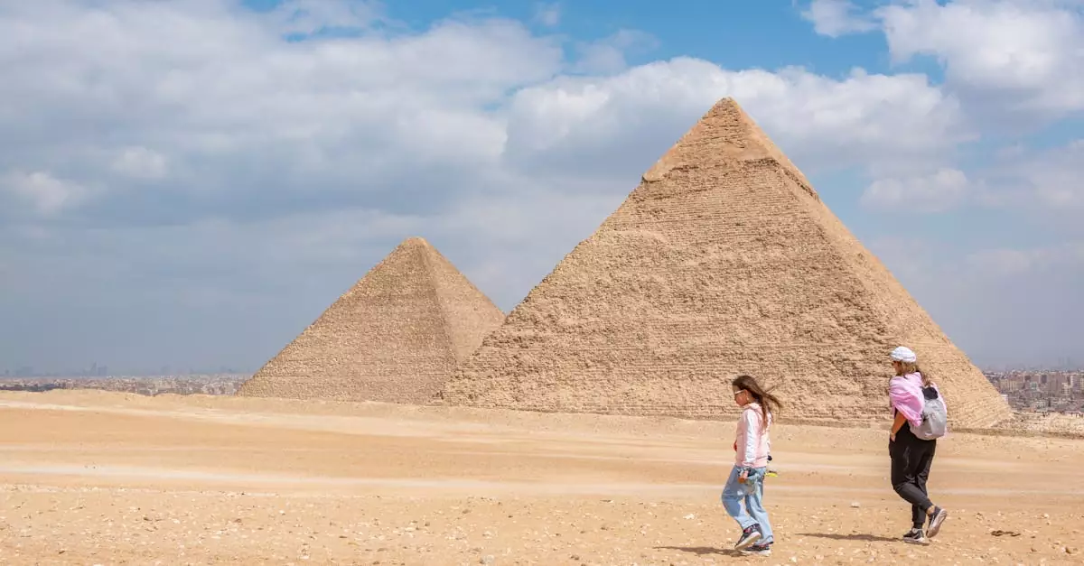 Two women walking near the iconic pyramids of Giza, Egypt, under a bright sky.