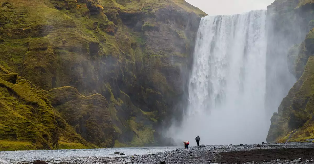 Two travelers admire the majestic Skógafoss waterfall in Iceland, surrounded by lush nature.