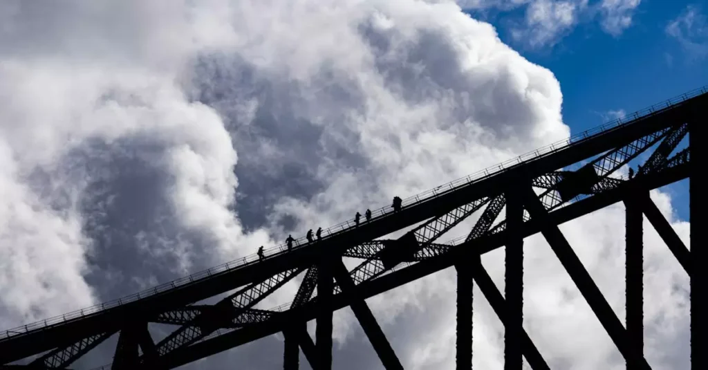 Climbable Bridges in Australia: Views & Adventures 5 Silhouetted climbers scale a steel bridge against a dramatic cloudy sky.