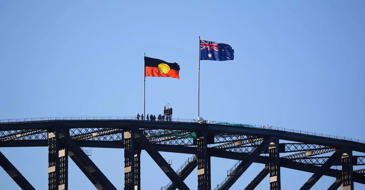 Sydney Harbour Bridge featuring the Australian and Indigenous flags waving against a clear blue sky.
