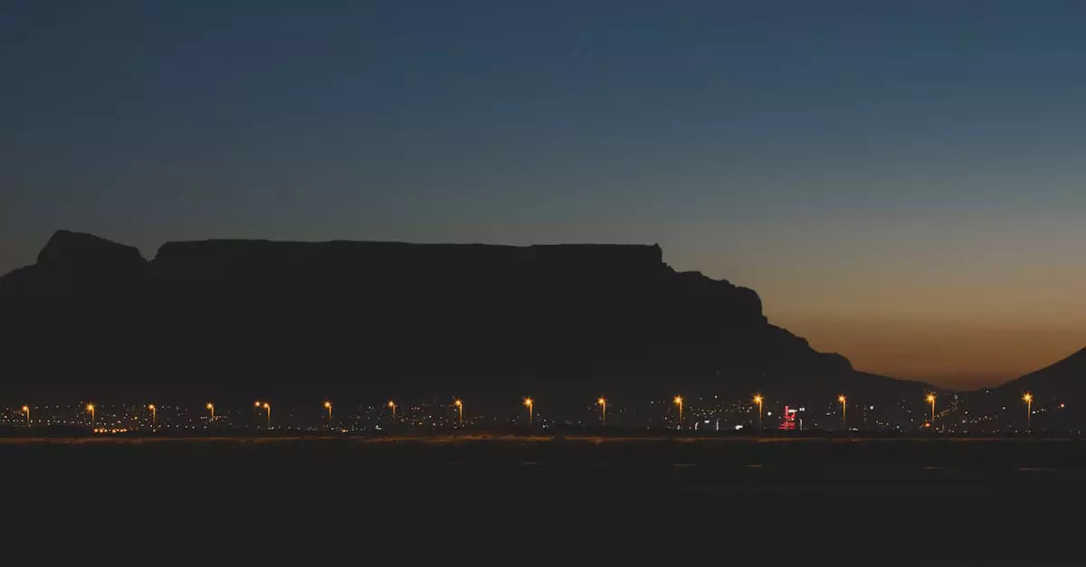 Silhouette of Table Mountain and city lights at dusk in Cape Town, South Africa.