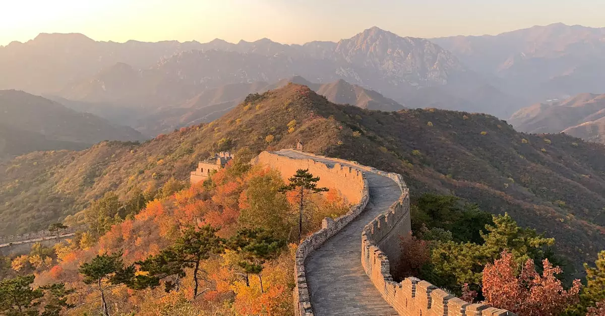 Great Wall of China going through hill with green trees with mountains behind on sunny day