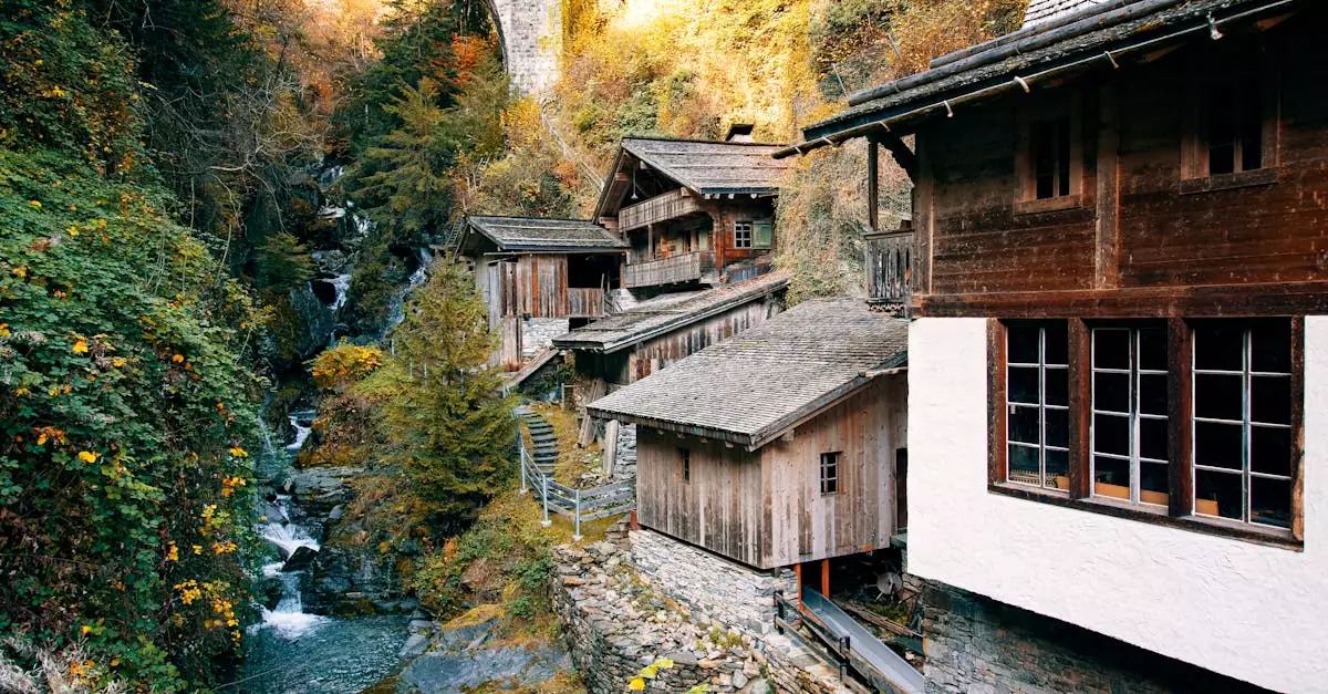 Charming wooden houses in a picturesque mountain village with autumn foliage and a stone bridge.