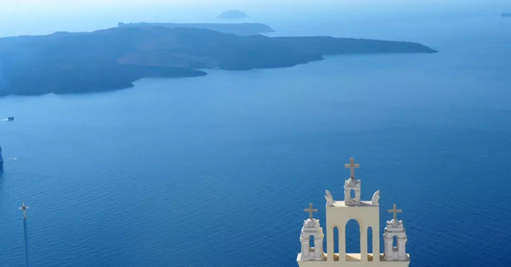 7 Hidden Greek Islands: Your Unforgettable Escape 2 Santorini church tower overlooking the Aegean Sea with distant islands in view.