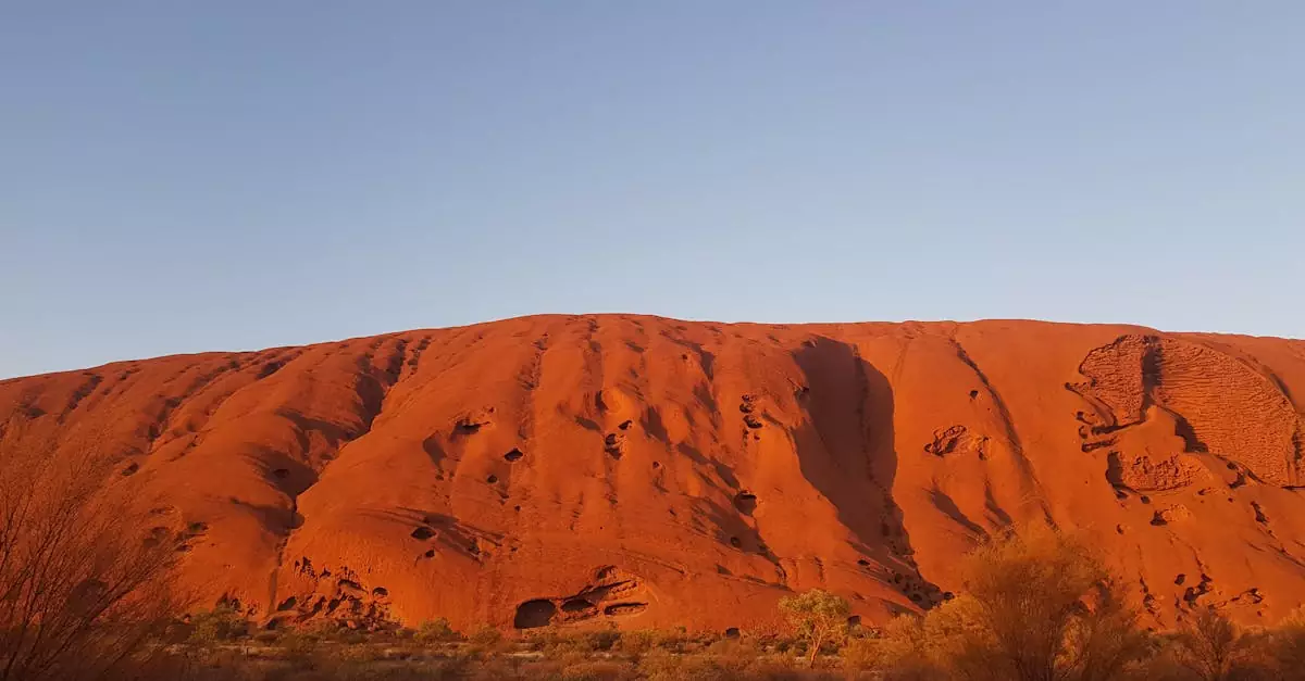 Stunning photo of Uluru with clear skies at sunrise, highlighting its iconic red sandstone.