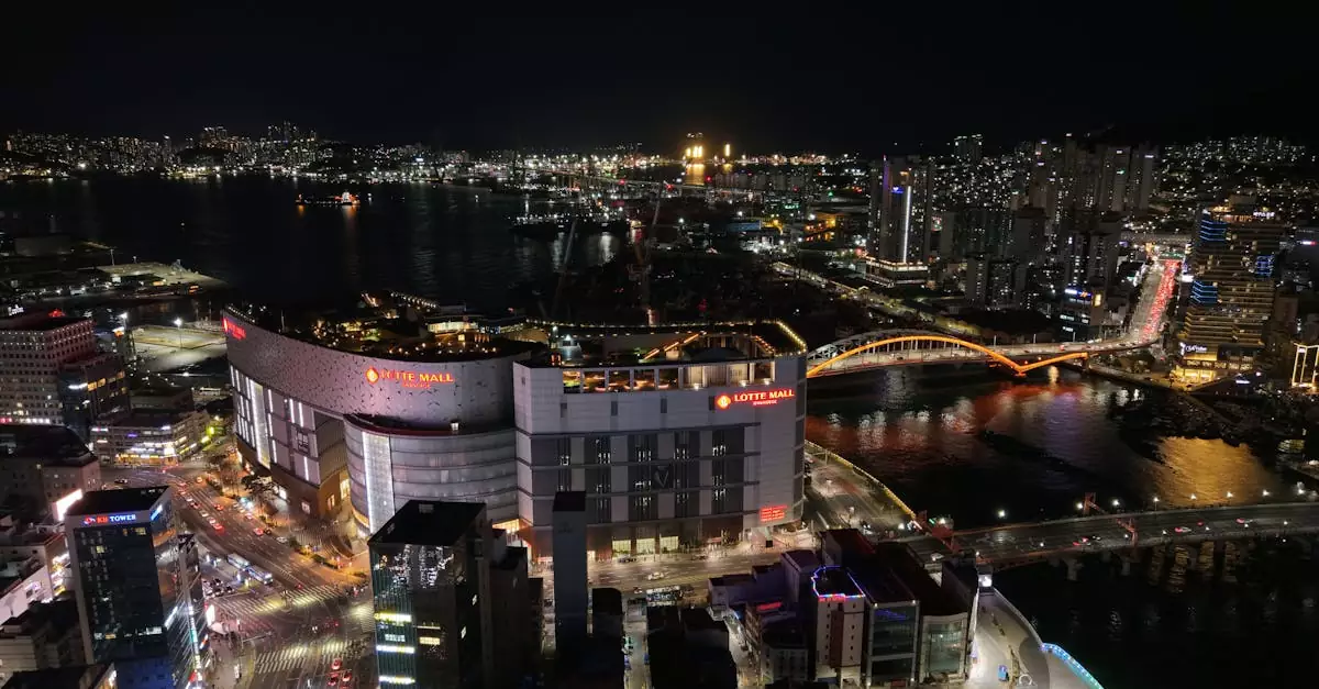 Aerial night view of Busan, South Korea featuring Lotte Mall and iconic bridges.