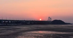 Captivating view of Yeongjong Bridge during sunset in Incheon, South Korea with serene waters and a warm orange sky.