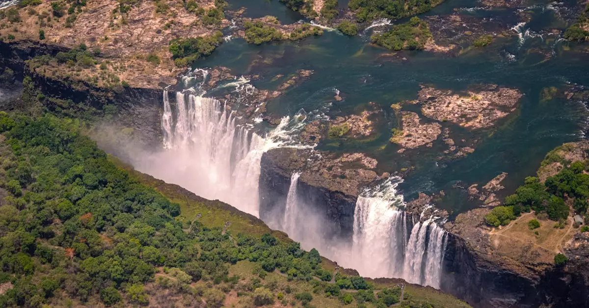 Breathtaking aerial view of Victoria Falls surrounded by lush greenery during summer day.