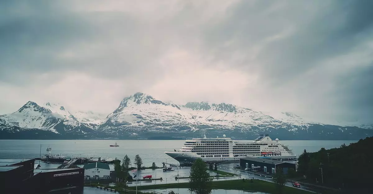 A cruise ship docked with snowy mountains in the background, under a cloudy sky.