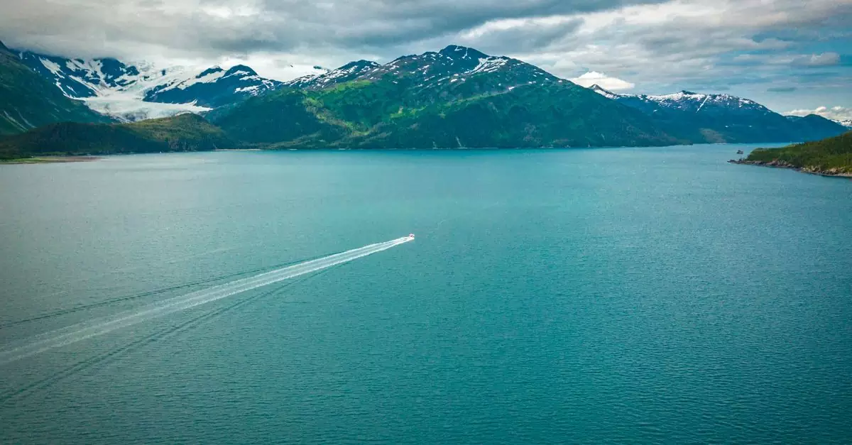Scenic aerial view of a lone motorboat cruising on a vast Alaskan lake with mountains.