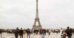Crowd of tourists at the iconic Eiffel Tower in Paris on an overcast day.