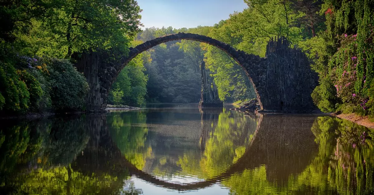 Capture of the iconic Rakotzbrücke reflecting in calm waters amidst lush greenery in Germany.