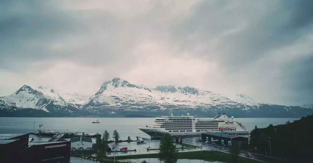 Best Alaska Cruises: Glaciers, Wildlife & Fjords Guide 2 A cruise ship docked with snowy mountains in the background, under a cloudy sky.