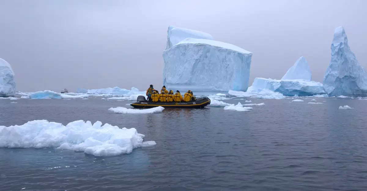An expedition group in a boat navigating icy waters near giant icebergs in Antarctica.