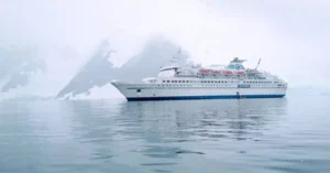 A cruise ship sails calmly through the icy waters of Antarctica, surrounded by snow-capped mountains.