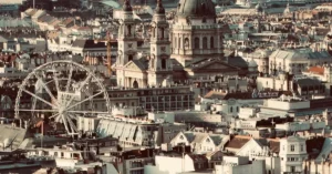 Aerial cityscape of Budapest featuring St. Stephen's Basilica and a Ferris wheel.