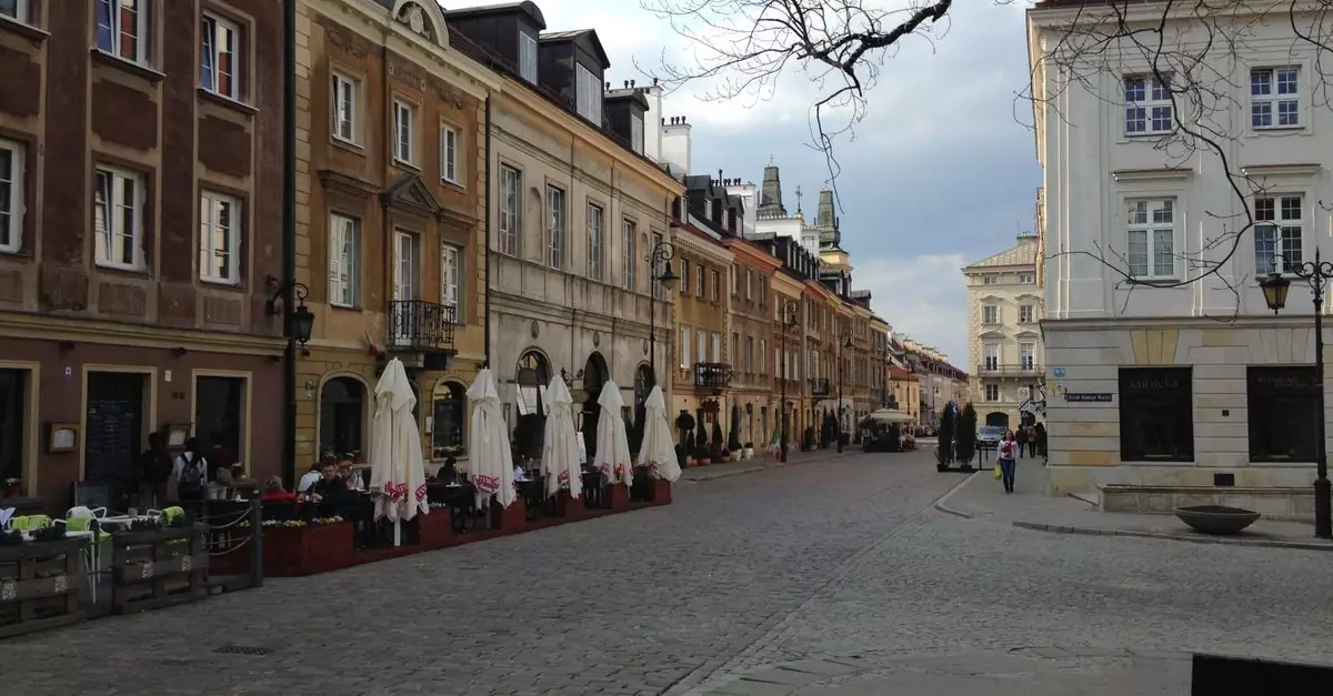 View of a historic street in Warsaw, Poland, featuring colorful architecture and outdoor cafes.