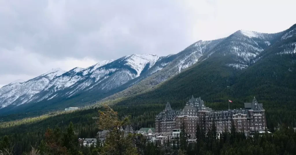 Best Canada Winter Escapes: Snowy Adventures 2 Scenic view of Banff Springs Hotel amidst snow-capped mountains and greenery.