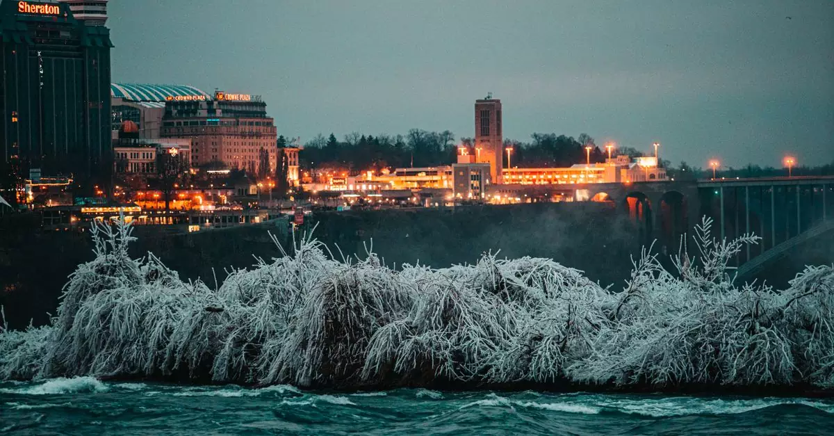Breathtaking winter scene of Niagara Falls with a view of icy trees and illuminated cityscape at twilight.