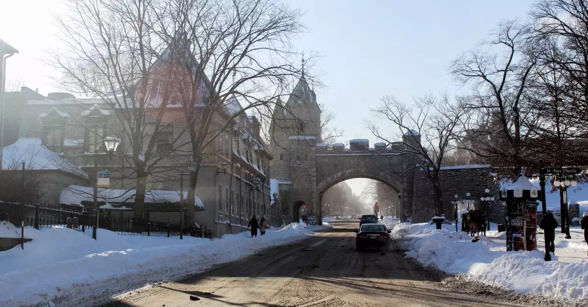 Snow-covered street scene in Old Quebec with a historic stone gate and winter landscape.