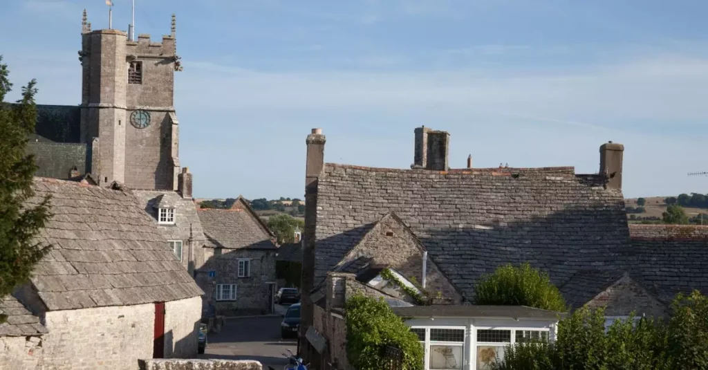 Best Castle Towns England: History & Charm 2 Charming view of historic rooftops and tower in Corfe Castle village, England.