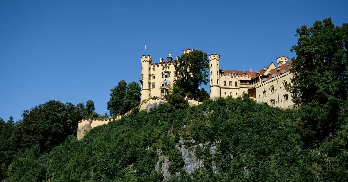 Scenic view of Hohenschwangau Castle atop a hill in F&uuml;ssen, perfect for travel and architecture enthusiasts.